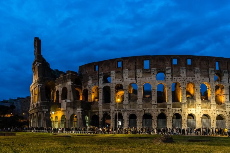 The colloseum by evening, still lines of people waiting to enter.